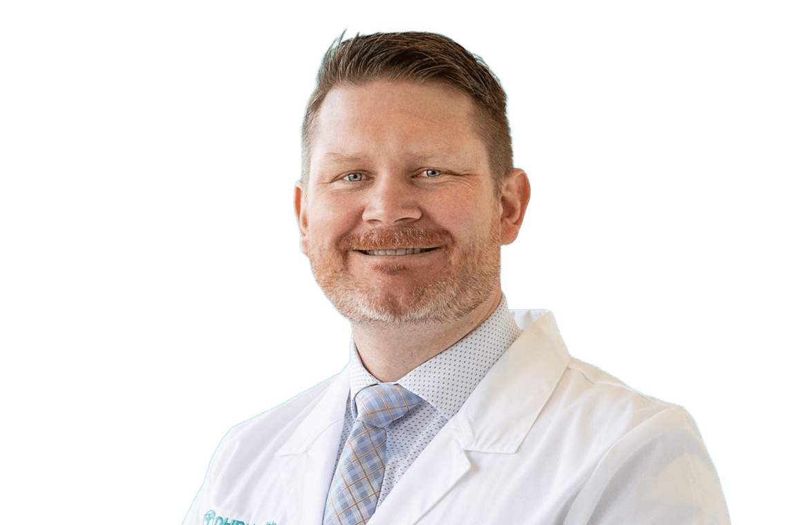 Smiling male doctor in a white coat and patterned tie against a teal background.