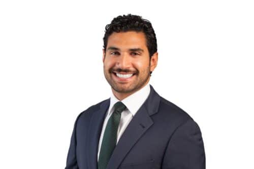 Professional headshot: smiling man in a navy suit and green tie against a white background, looking at the camera.