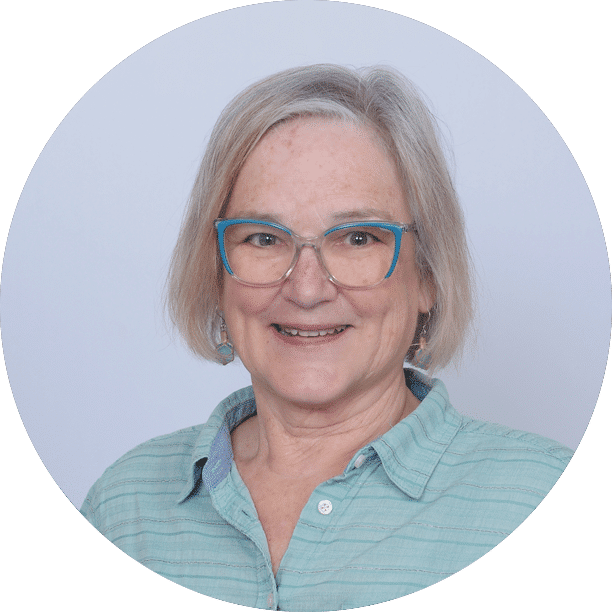 Debbie-Davis-Bio-Pic-nb - Coloplast Men's Health Smiling woman with short gray hair and blue glasses, wearing a light teal button-up shirt (circular portrait).